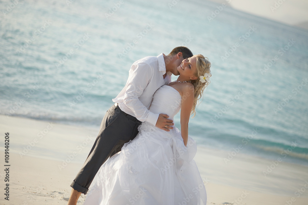 Beautiful young couple kissing on sunset, standing barefoot on b Beautiful young couple kissing on sunset, standing barefoot on b