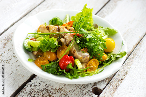 Delicious salad with grilled chicken breast on a wooden background