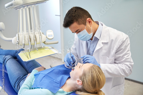 male dentist in mask checking female patient teeth