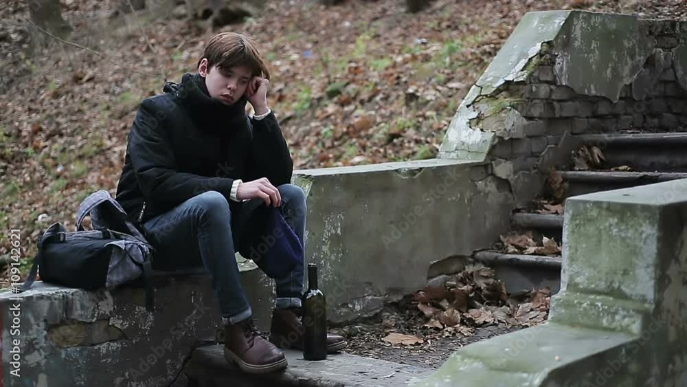 Teenager having troubles, sitting in park alone with bottle of alcoholic drink Teenager having troubles, sitting in park alone with bottle of alcoholic drink