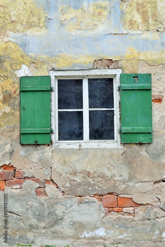 Geöffnete grüne Fensterläden aus Holz an einem sanierungsbedürftigen Gebäude mit offenem Mauerwerk