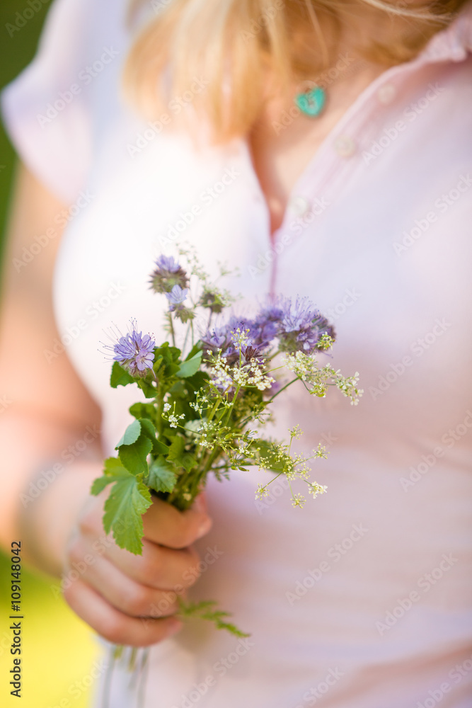 Young blond woman in pink holding a beautiful garden flowers in her hand. Summer bouquet in girl's hand. Outdoor. Spring garden present. Person with bunch of flowers.