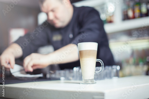 Barista prepares cappuccino in his coffee shop. Close-up cup of coffee.