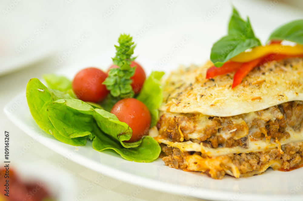 Closeup elegant serving of lasagne and small salad sitting on white plate Closeup elegant serving of lasagne and small salad sitting on white plate