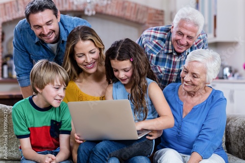 Multi-generation family sitting on sofa and using laptop