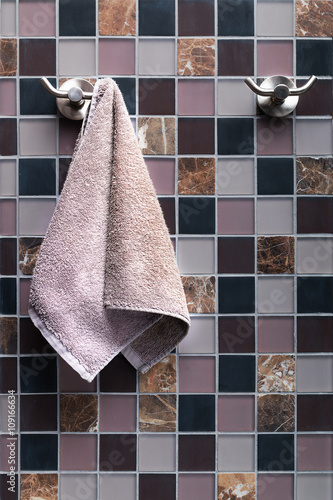 Tableau sur toile Small lilac terry towel for hands hanging on a towel rack in the bathroom on a square lined ceramic tile background