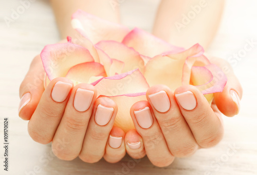 Woman hands with beautiful rose  petals on wooden background, close up