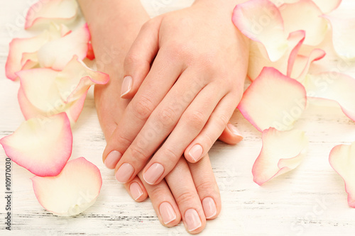 Woman hands with beautiful rose petals on wooden background, close up