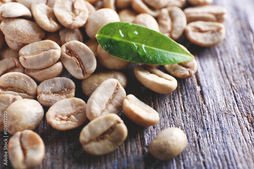 Obraz premium Green coffee beans with a leaf on wooden table