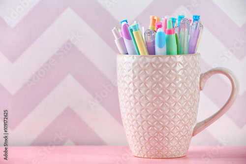 Pens in ceramic cup, pencils and markers on color background © Africa Studio