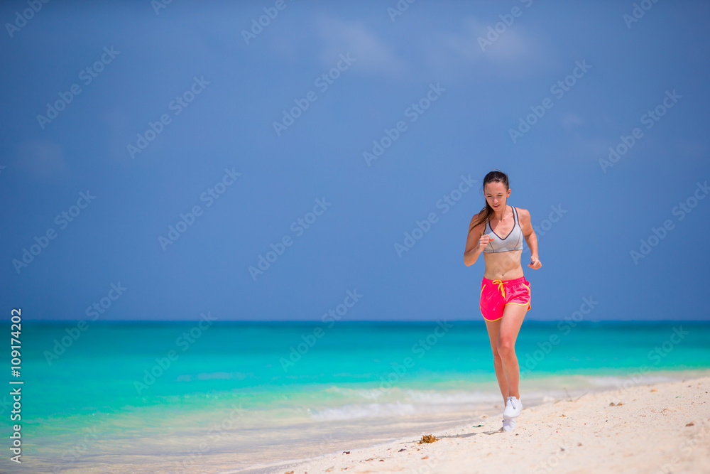 Fit young woman running along tropical beach in her sportswear 