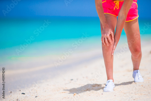 Female athlete suffering from pain in leg while exercising on white beach