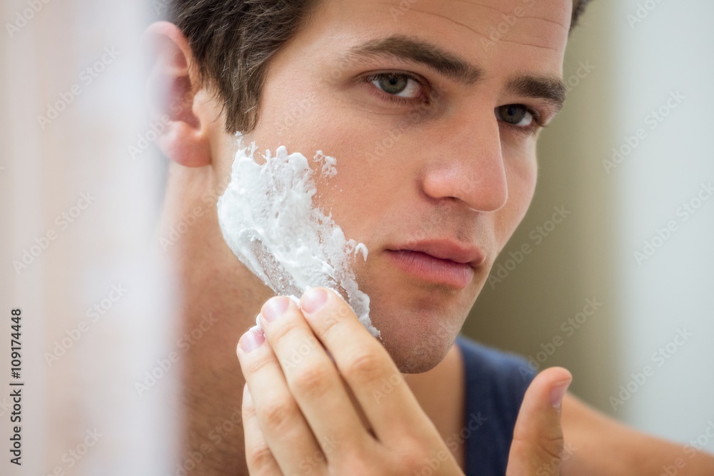 Young man applying shaving foam on his face