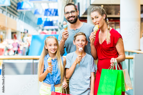 Family eating ice cream in shopping mall with bags