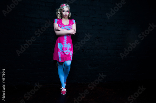 Beautiful blonde girl with two pigtails, with creative doll make-up: pink glossy lips, wearing pink skeleton dress. for the Halloween party. Posing like a doll. Studio shot, retouched image.