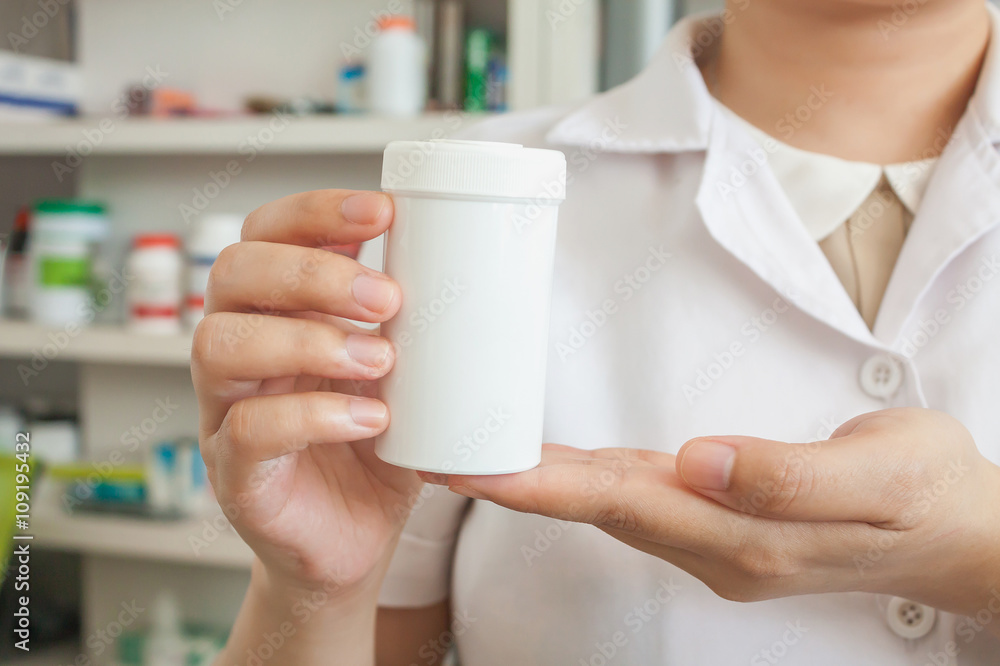 Pharmacist showing medicine bottle on her hand in the pharmacy Pharmacist showing medicine bottle on her hand in the pharmacy