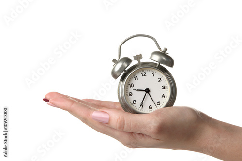 the woman holds in her hand a silver wind-up alarm clock over white isolated background