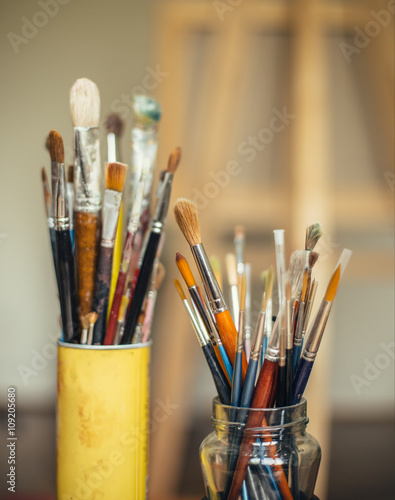 Paintbrushes in two jars with easel in background