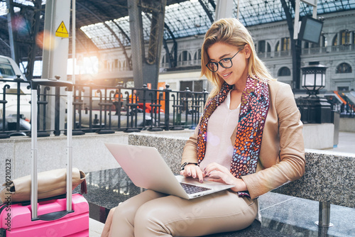 Beautiful Caucasian woman using net-book while sitting in train station interior. modern businesswoman using a laptop computer while waiting for the train. Flare light.