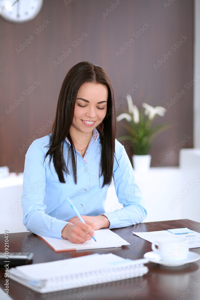 Young business woman sitting and writing at the table in office Young business woman sitting and writing at the table in office
