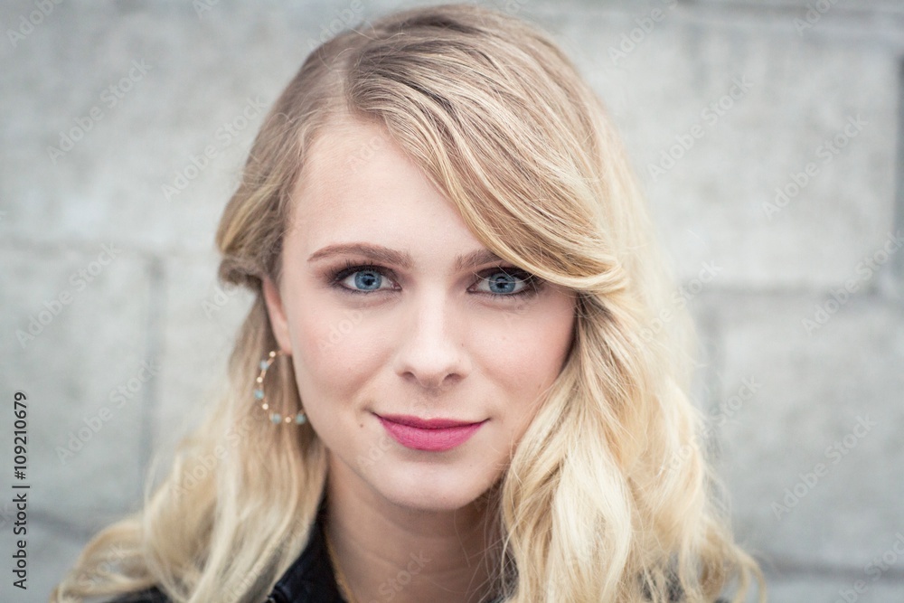 Young blonde haired woman in front of breeze block wall looking at camera smiling Young blonde haired woman in front of breeze block wall looking at camera smiling