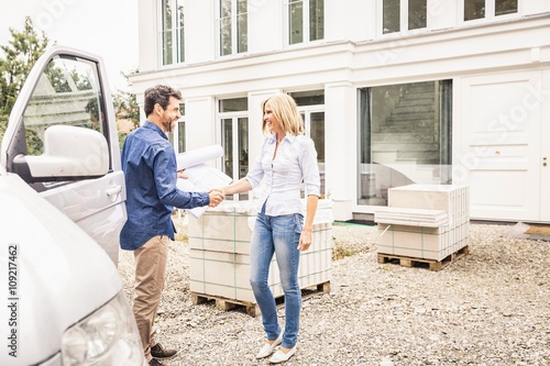 Builder arriving in van, shaking hands with homeowner smiling