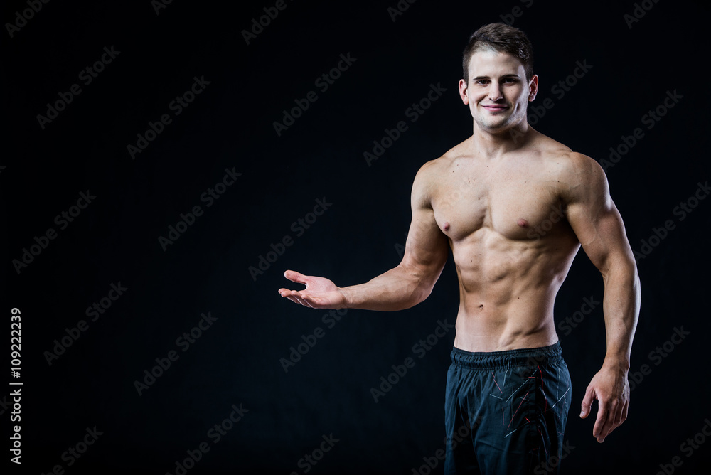 Shirtless muscular athletic man point with one hand to blank copyspace. Sexy bodybuilder showing his body on black isolated background copy space.