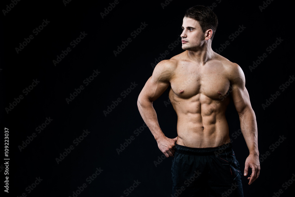 Young and fit male model posing his muscles looking to the left isolated on black background with copyspace