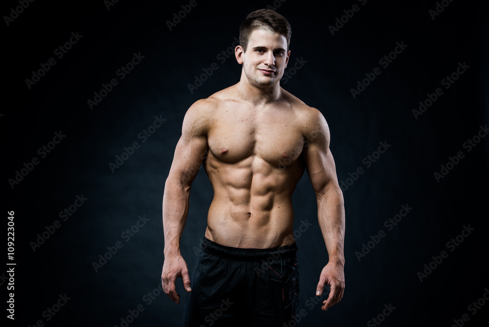 Muscular male model bodybuilder looking straight to the camera. Isolated on black.