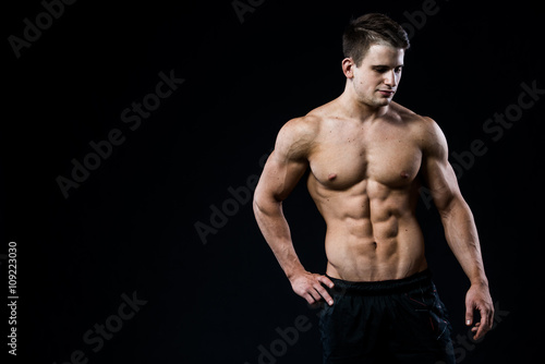 Young and fit male model posing his muscles looking downwards isolated on black background