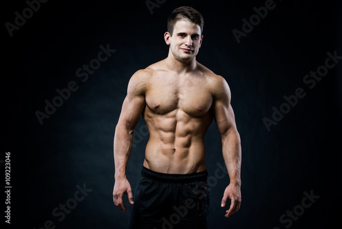 Muscular male model bodybuilder looking straight to the camera. Isolated on black.