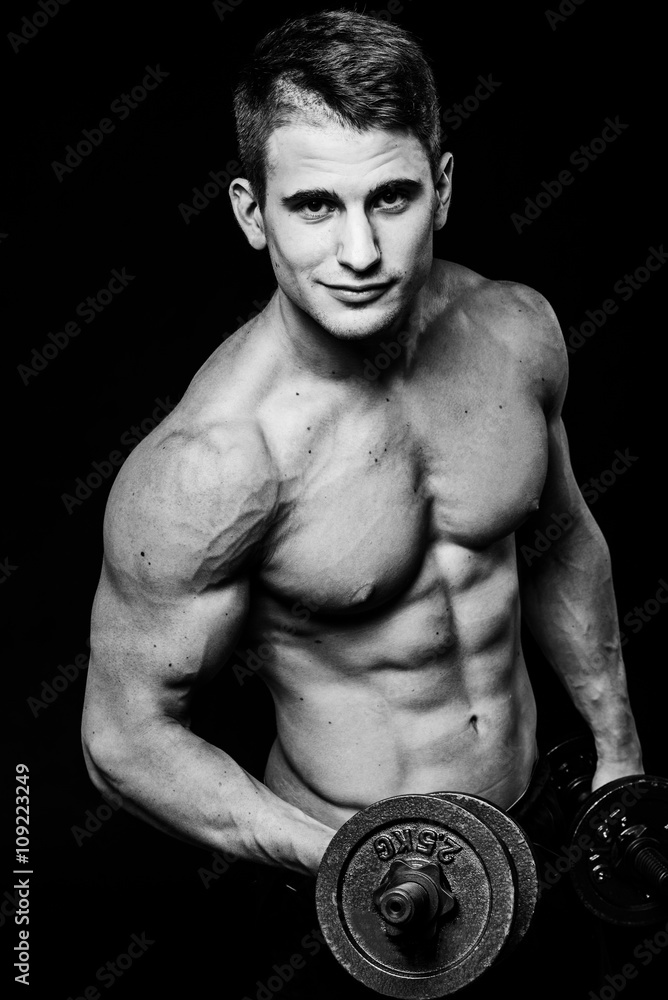 Dark black and white contrast shot of young muscular fitness man stomach arm. Working out with dumbbells isolated Dark black and white contrast shot of young muscular fitness man stomach arm. Working out with dumbbells isolated