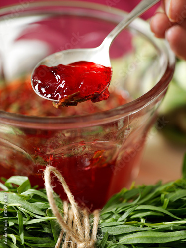Woman fingers holding spoon in jar of homemade redcurrant jam photo