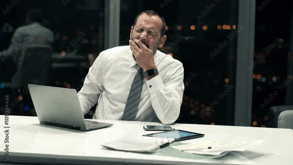 Tired businessman with laptop yawning in the office during night
