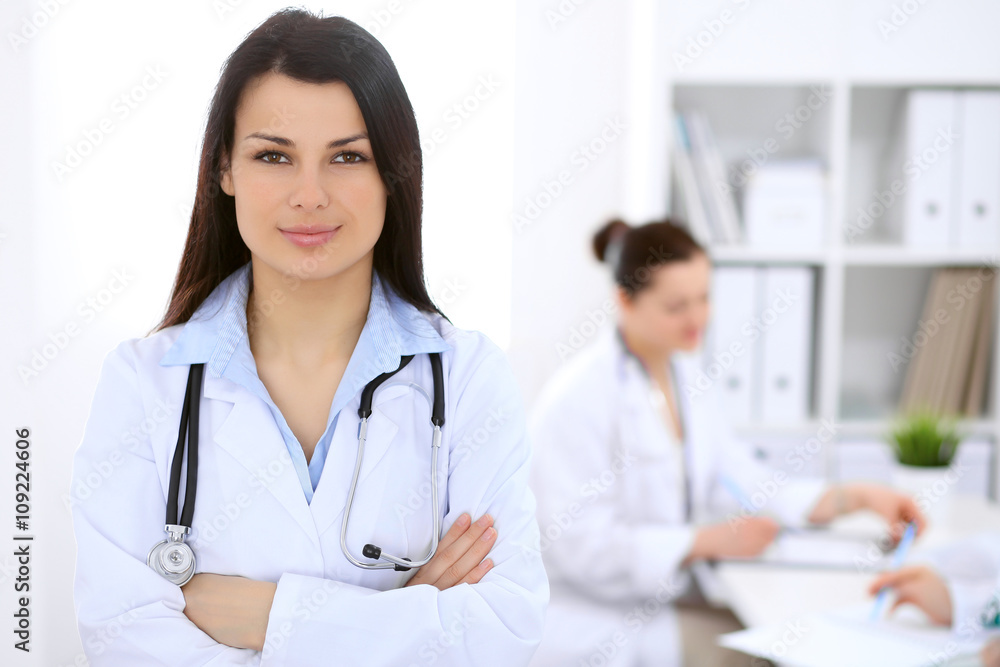 Brunette female doctor on the background of colleagues talking to each other in hospital Brunette female doctor on the background of colleagues talking to each other in hospital
