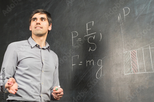 Obraz na plátně Portrait of young happy smiling teacher man standing near chalkboard with mathem