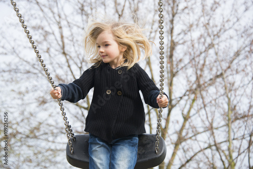 Little child blond girl having fun on a swing outdoor. Summer playground. Girl swinging high 