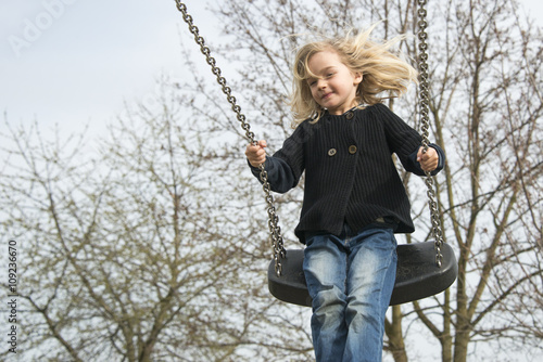 Little child blond girl having fun on a swing outdoor. Summer playground. Girl swinging high 