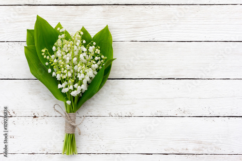 Obraz na plátně bouquet of lilies of the valley flowers with green leaves tied with twine in the water droplets on the white wooden boards