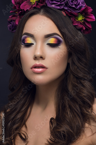 Closeup portrait of beautiful woman with colorful makeup on eyes and flowers on head