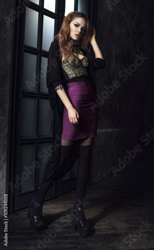 Sexy young woman in violet skirt standing in vintage dark interior