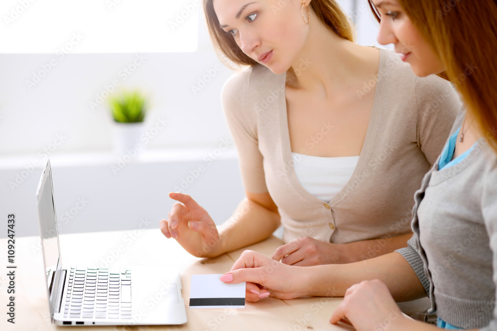 Two friends or sisters talking taking a conversation at the table with laptop looking each other Two friends or sisters talking taking a conversation at the table with laptop looking each other