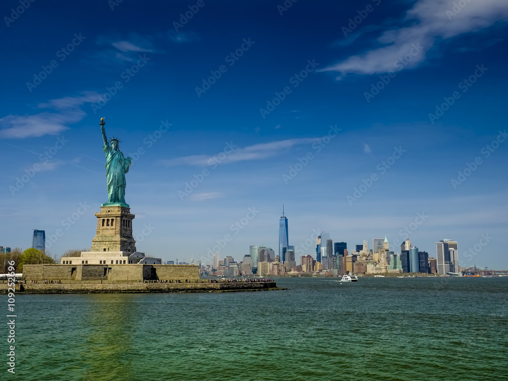 Fototapeta premium Statue of Liberty on a sunny day, Manhatten in the background. This is a photo-montage, because the statue faces to the viewer!