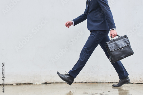 A man in a suit with a briefcase in hand comes against the backdrop of a white wall photo