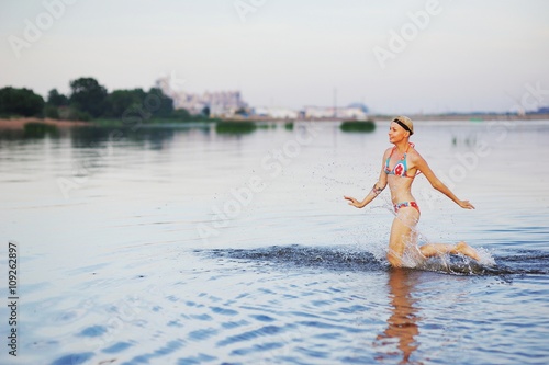 Girl runs into water in swimsuit. Beauty Model Girl Splashing Water with her legs. Beautiful Woman in Water