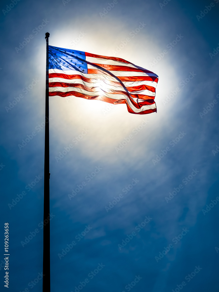 American flag on the blue sky in front of the sun, sun is shining through  the flag Stock Photo