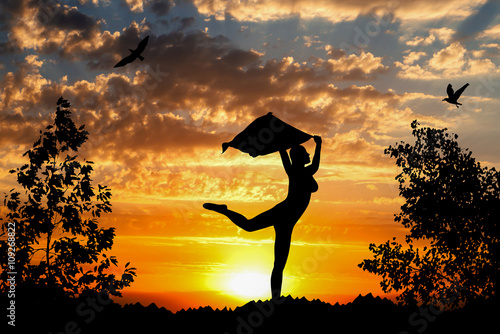 Young girl silhouette with shawl dancing on golden cloudy sunset background
