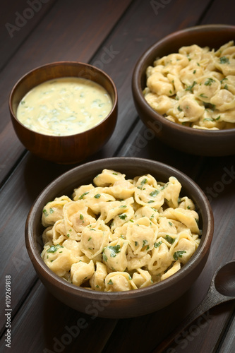 Cooked tortellini stuffed with cheese served with parsley cream sauce in rustic bowl, photographed on dark wood with natural light (Selective Focus, Focus one third into the dish)