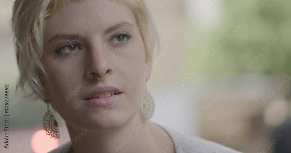 Big close up of young woman with blonde hair and big ear-rings listening, thinking and being serious in urban exterior setting. Hand-held camera recorded at 60fps. Big close up of young woman with blonde hair and big ear-rings listening, thinking and being serious in urban exterior setting. Hand-held camera recorded at 60fps.