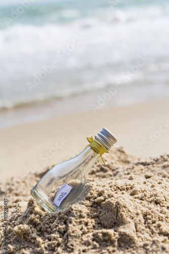 SOS message in glass bottle on the beach. © skarie